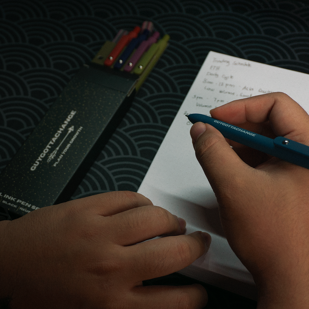 Hand writing a schedule with GuyGottaChange black gel pen next to 5-piece pen set box
