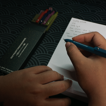Hand writing a schedule with GuyGottaChange black gel pen next to 5-piece pen set box