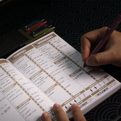 Filling in weekly planner spread with GuyGottaChange pink gel pen showing daily goals and productivity tracker