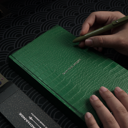 Hand holding green GuyGottaChange gel pen on green textured Plan Your Growth planner cover