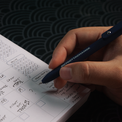 Close-up of GuyGottaChange branded black gel pen writing in weekly planner
