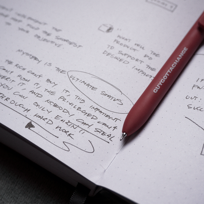 Red GuyGottaChange branded gel pen resting on notebook with handwritten mind map and planning notes